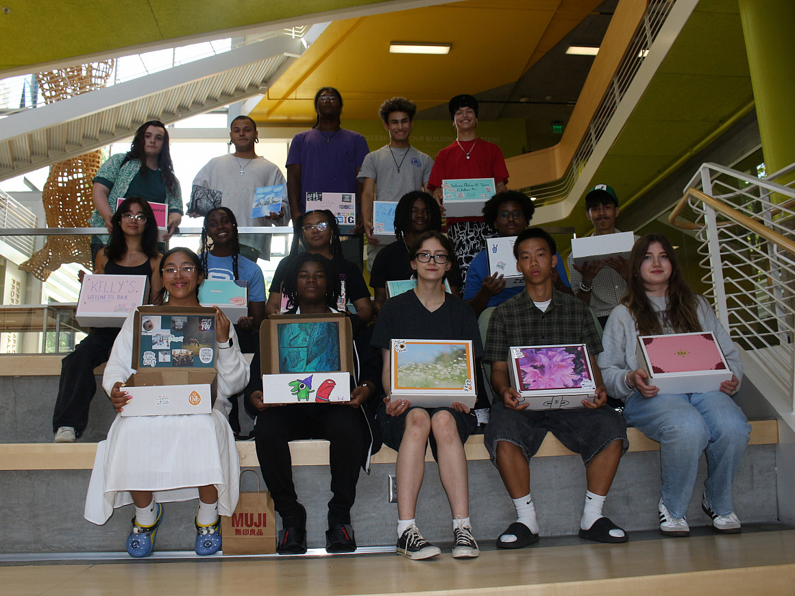 Group of students sitting and holding open boxes filled with wellness items.