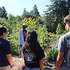 Students standing outside on a farm, listening to a man talk.