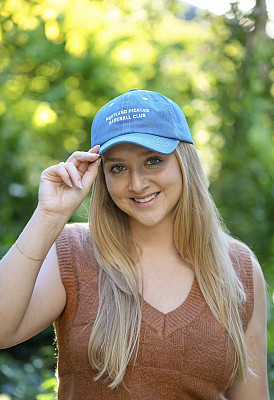 An alumna wearing a blue Pickles hat and smiling at the camera.