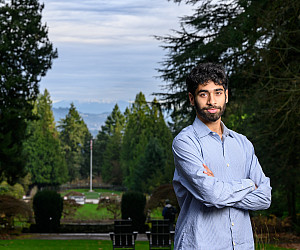 Ishan posing outside wearing a blue shirt, surrounded by green trees.