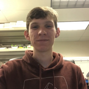 Jack Waite BA '23 selfie. He is wearing a brown hoodie with a white outline drawing of two mountains.