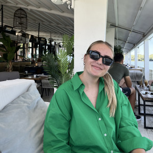 Sara smiling at the camera, wearing sunglasses and a green button-up shirt.