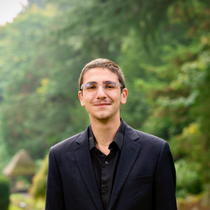 Elie smiling outside wearing a black shirt and black jacket.