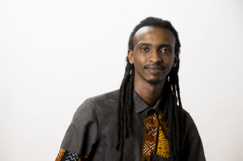 Rene smiling at the camera, wearing a black, brown, and yellow collared shirt.