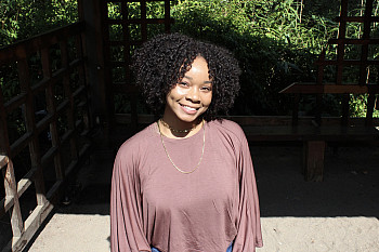 Nichole smiling at the camera outside, wearing a brown top.