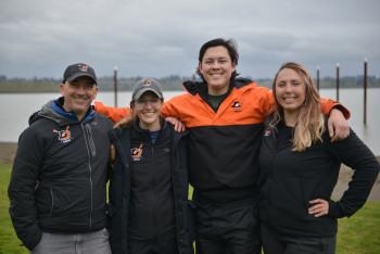 Four women's rowing coaches standing together with arms around each other smiling