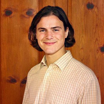 Aidan smiling at the camera, wearing a white button-up top.