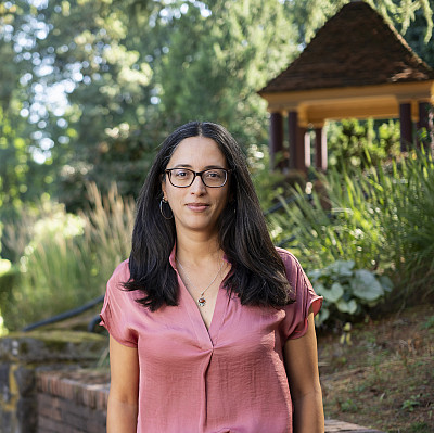 Heidi posing outside, wearing a pink top and glasses.